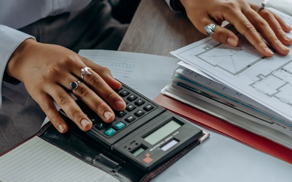 Person calculating project costs while reviewing floor plans