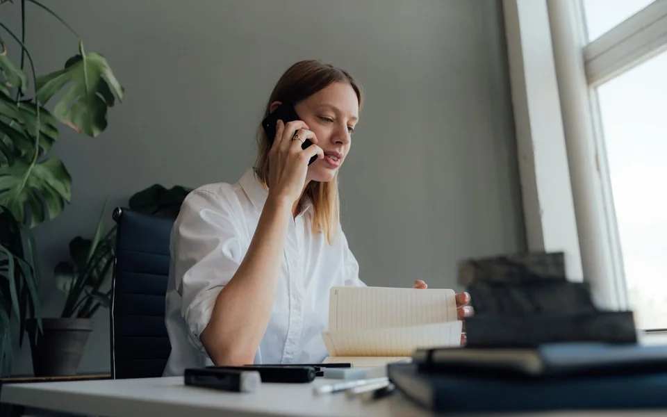 Businesswoman speaking on the phone while reviewing notes at her desk