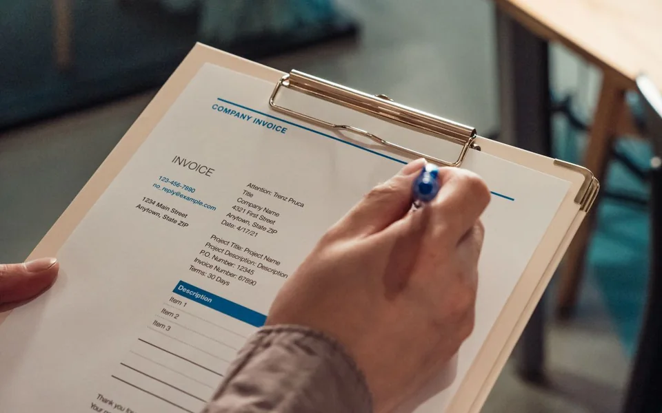 Person reviewing an invoice on a clipboard with a pen
